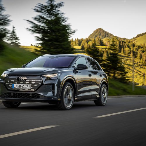 Audi Q4 SUV e-tron in Tamboragrey, outdoor driving shot, exterior, three-quarter front view on a winding road in an alpine landscape.
